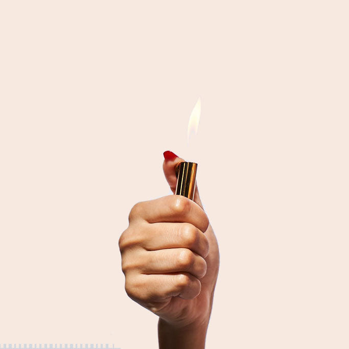 Hand holding a lit lipstick against a plain background