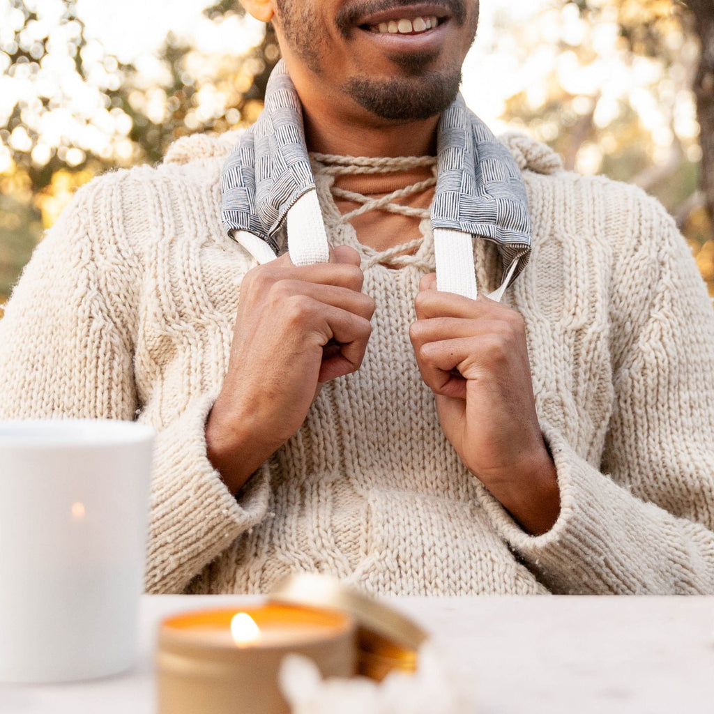 Man wearing a beige sweater and gray neck wrap a white mug outdoors with blurred background