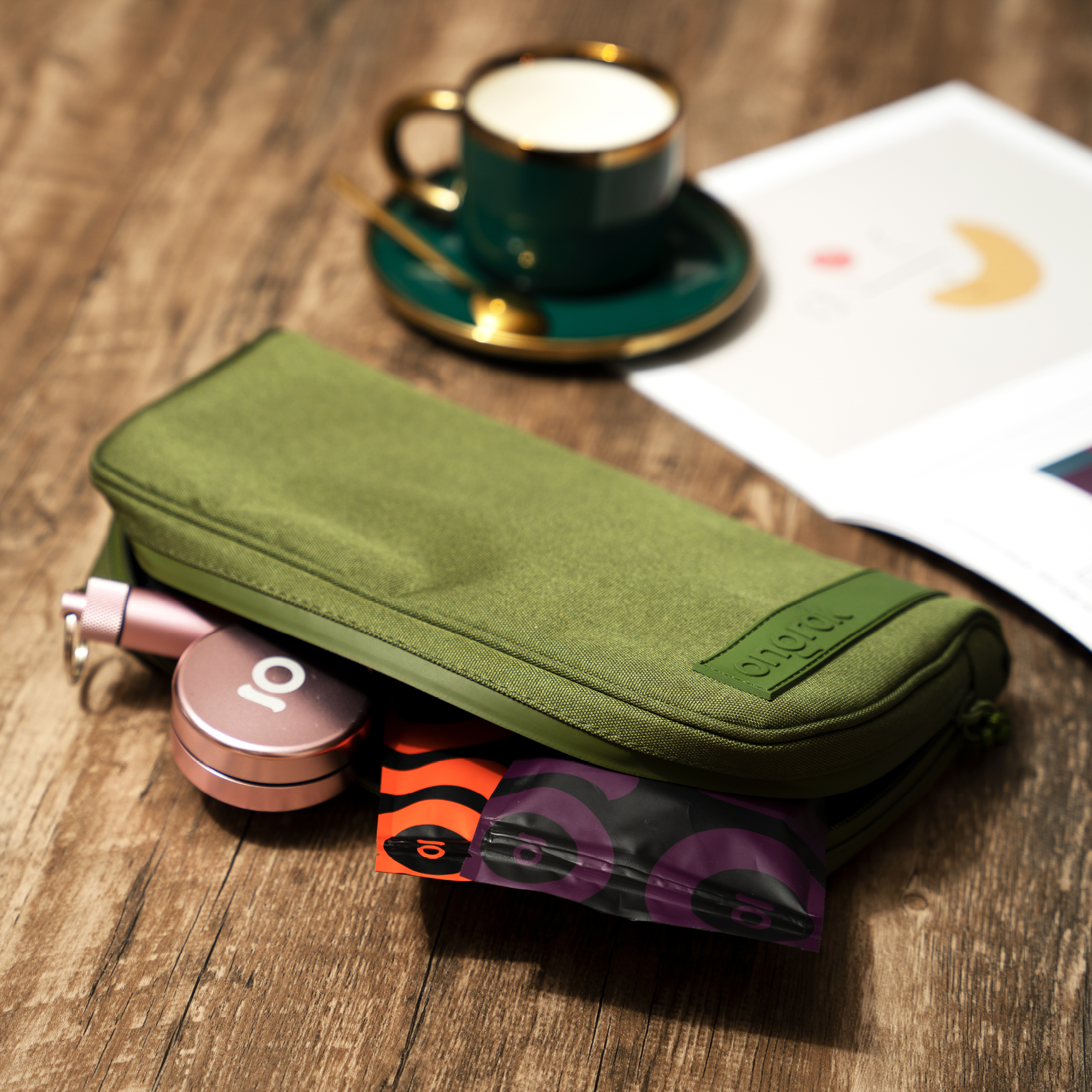 Green travel pouch with toiletries on a wooden surface with a cup of coffee in the background