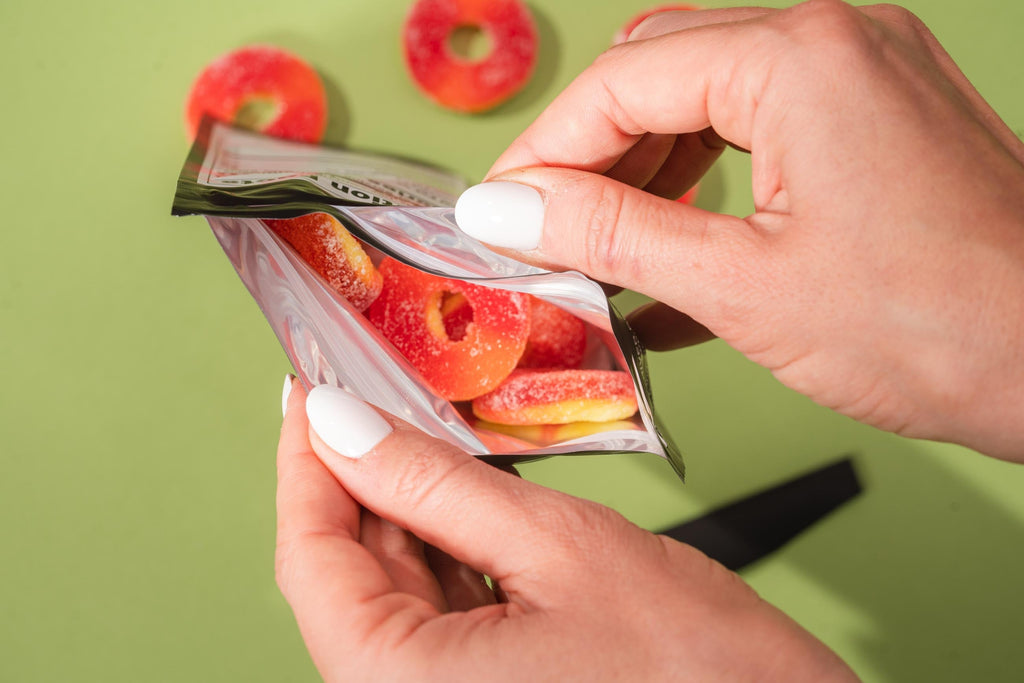 Hand holding a package of colorful gummy candies against a green background