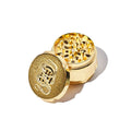 Gold-colored herb grinder with a brand logo on a white background