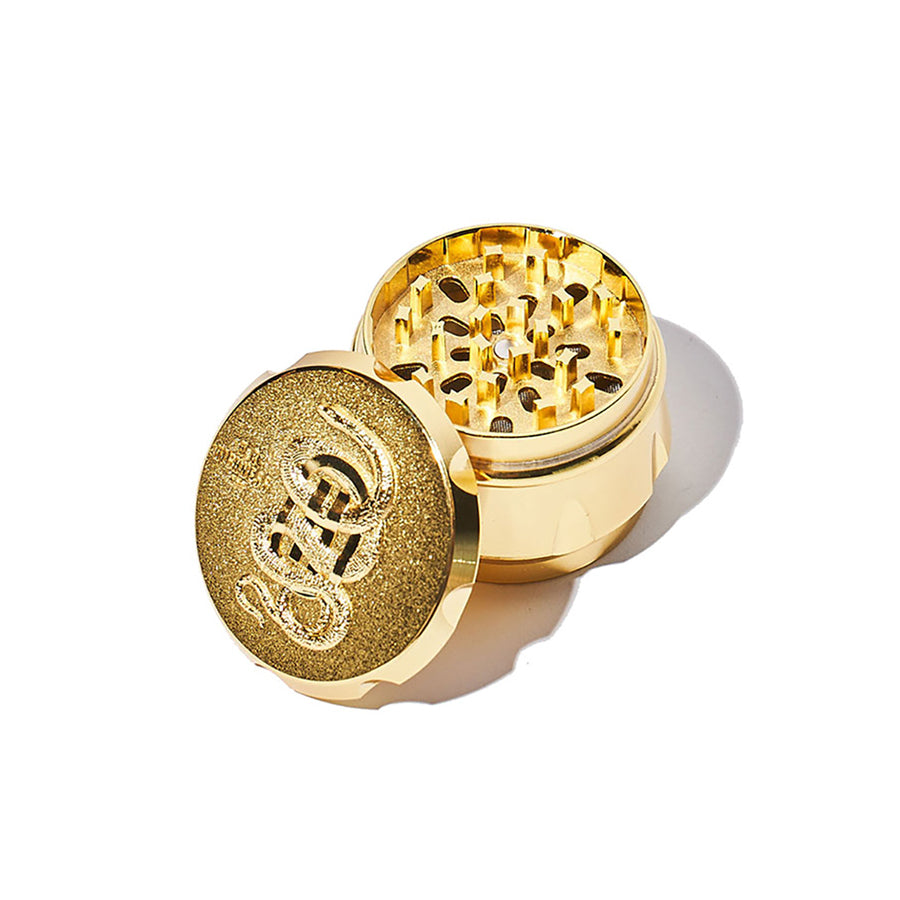 Gold-colored herb grinder with a brand logo on a white background