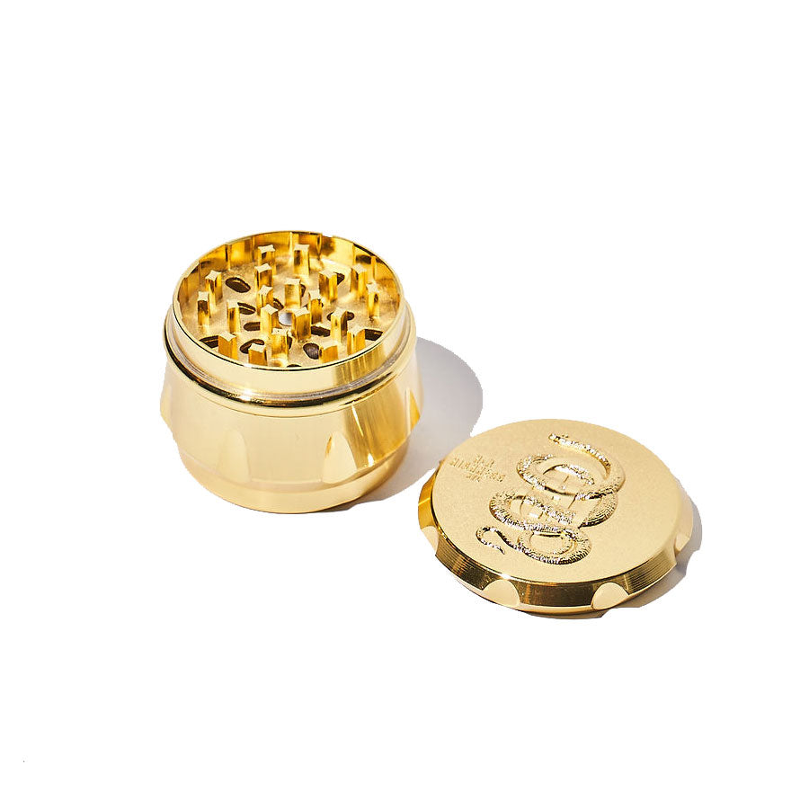 Gold-colored herb grinder with a branded lid on a white background