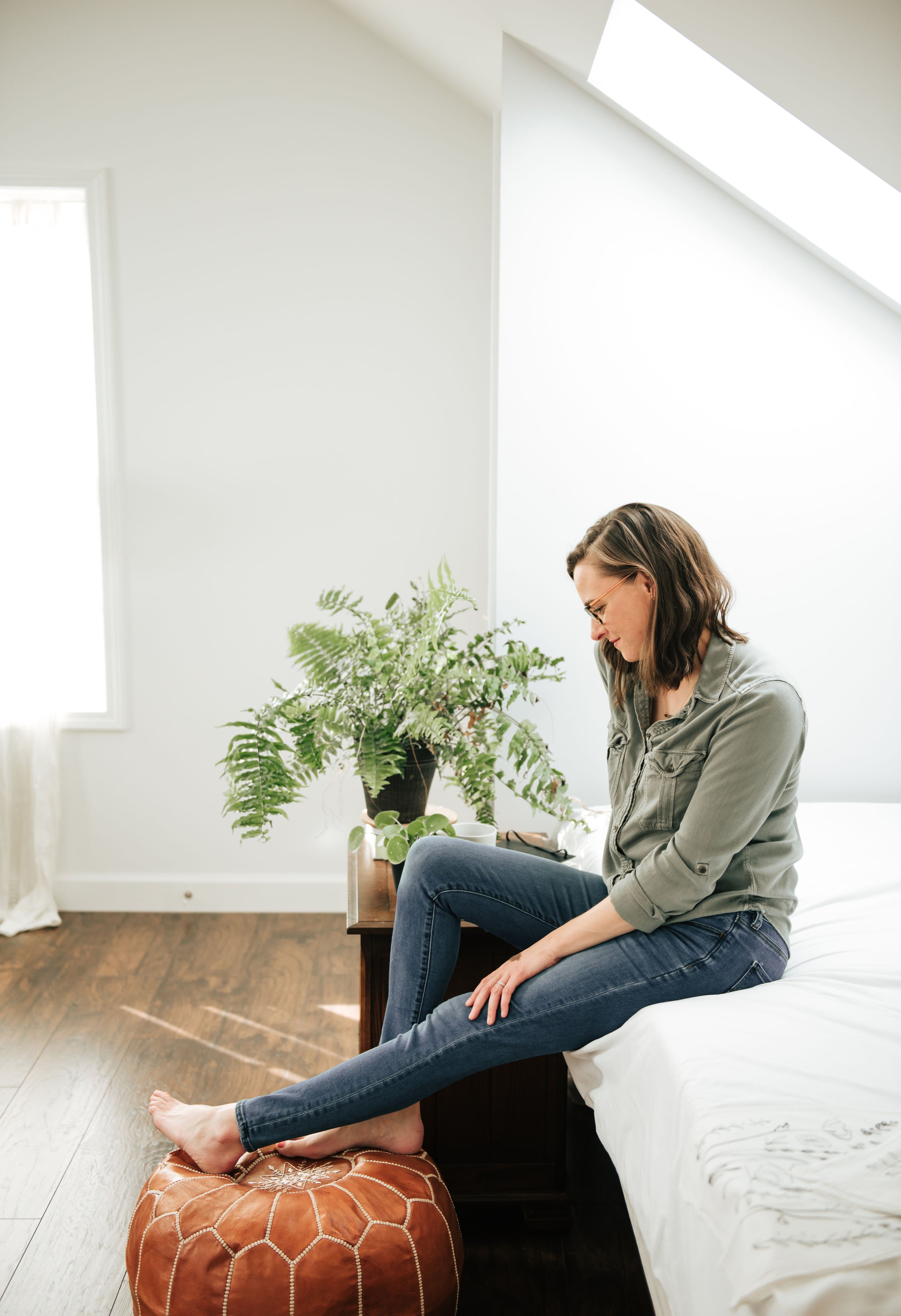 Woman sitting on a leather ottoman in a modern living room with a plant and white walls.