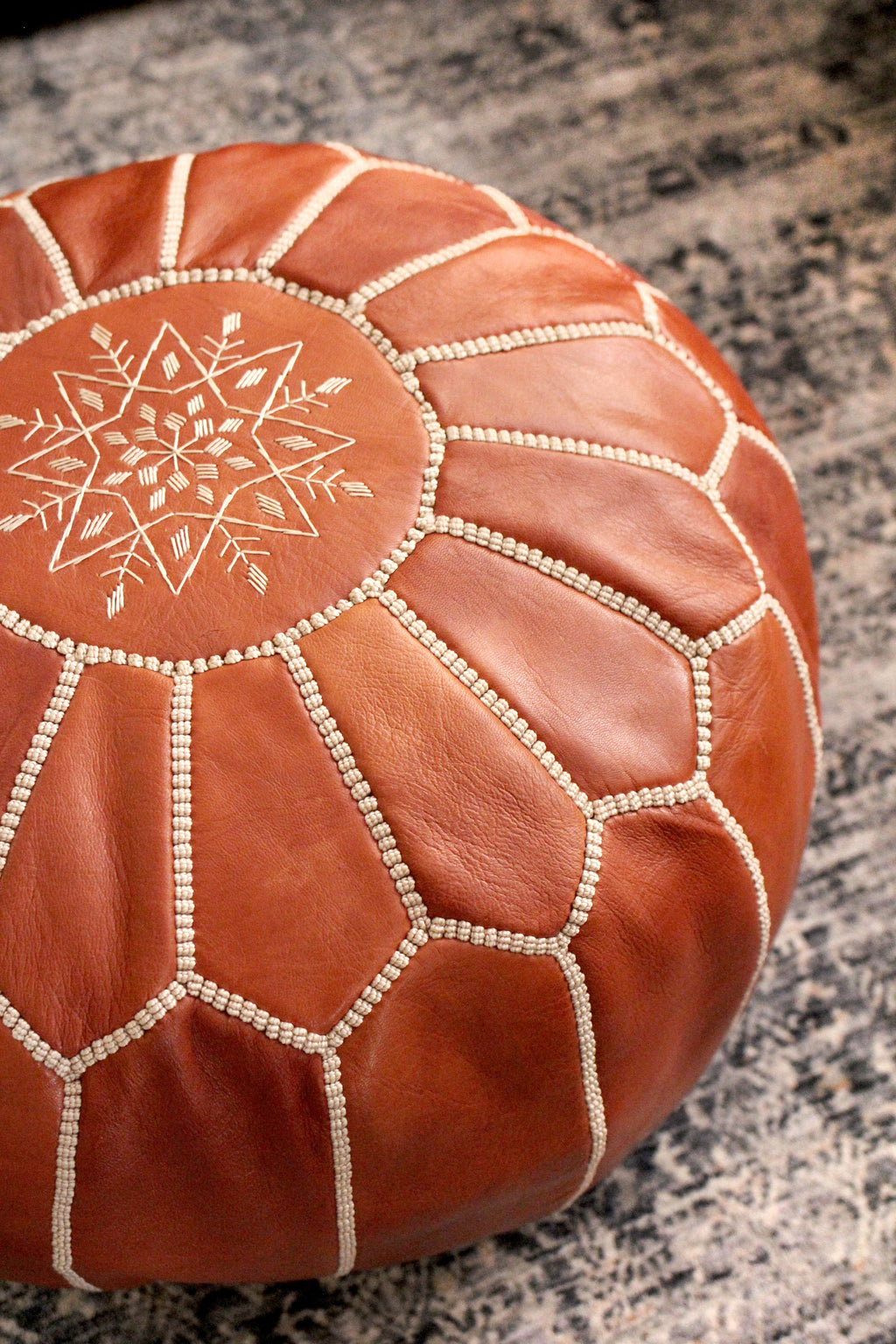 Brown leather ottoman with decorative patterns on a textured surface
