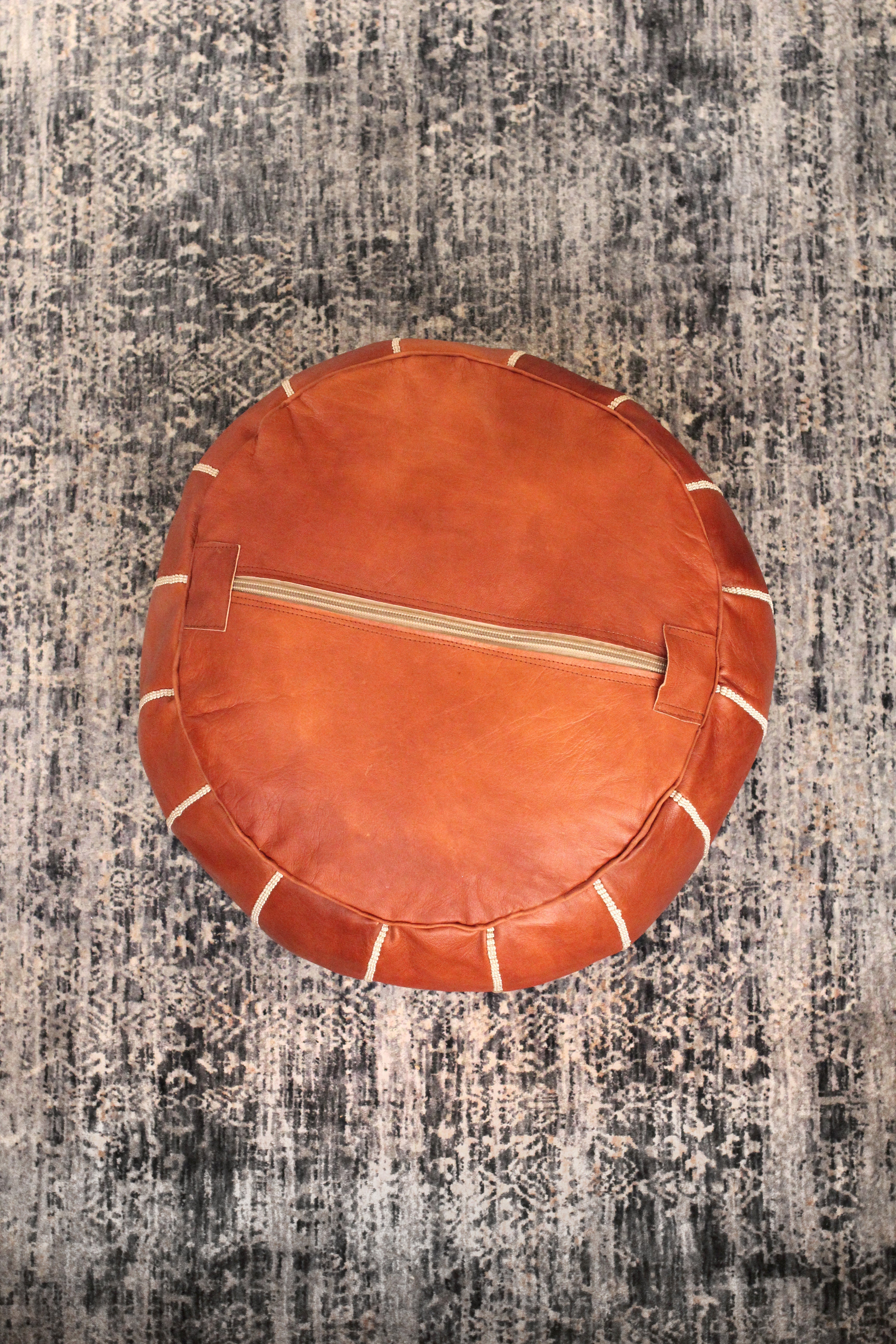 Round brown leather pillow with a zipper on a textured gray surface