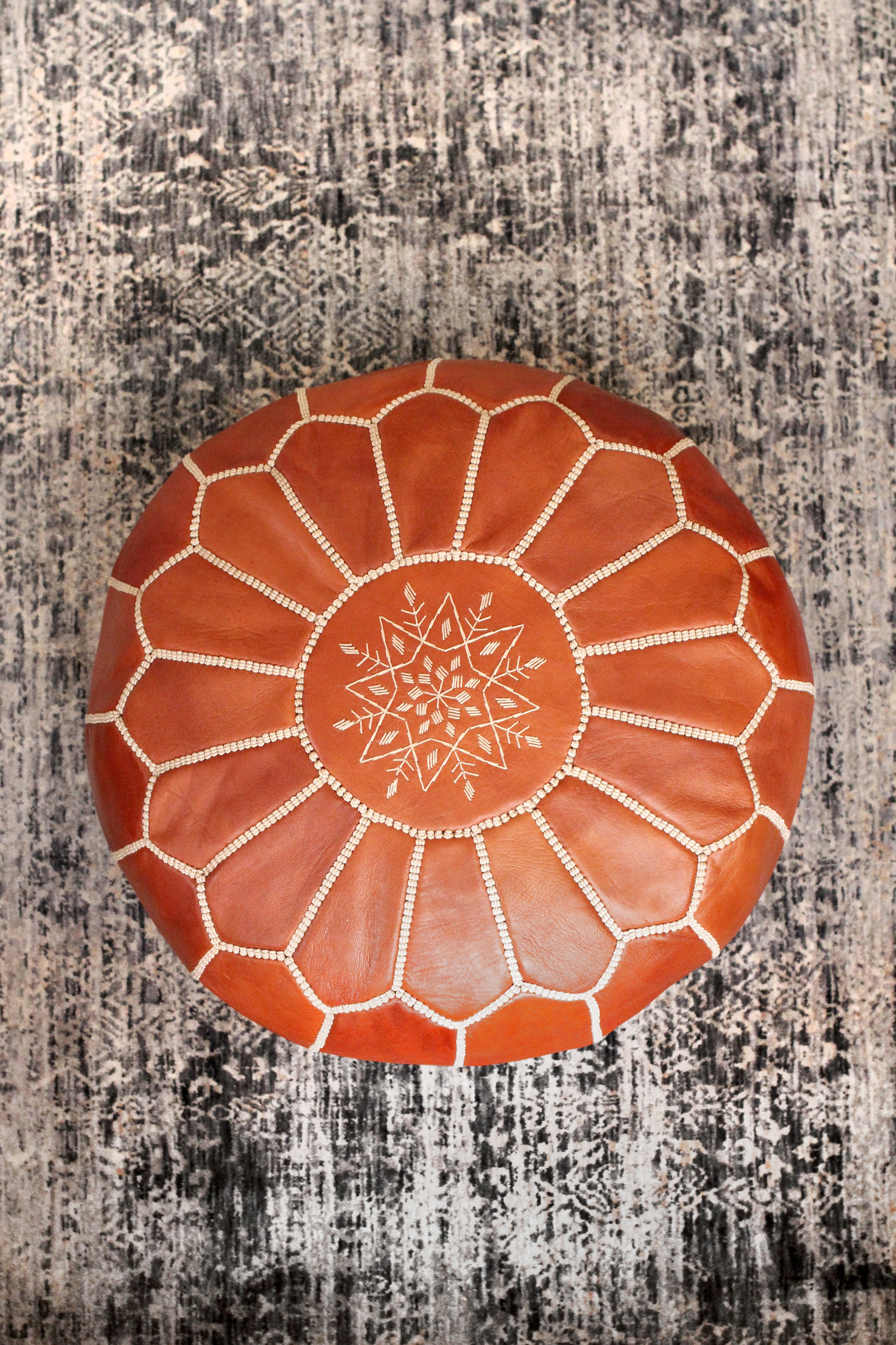 Round brown leather ottoman with star design on a textured surface