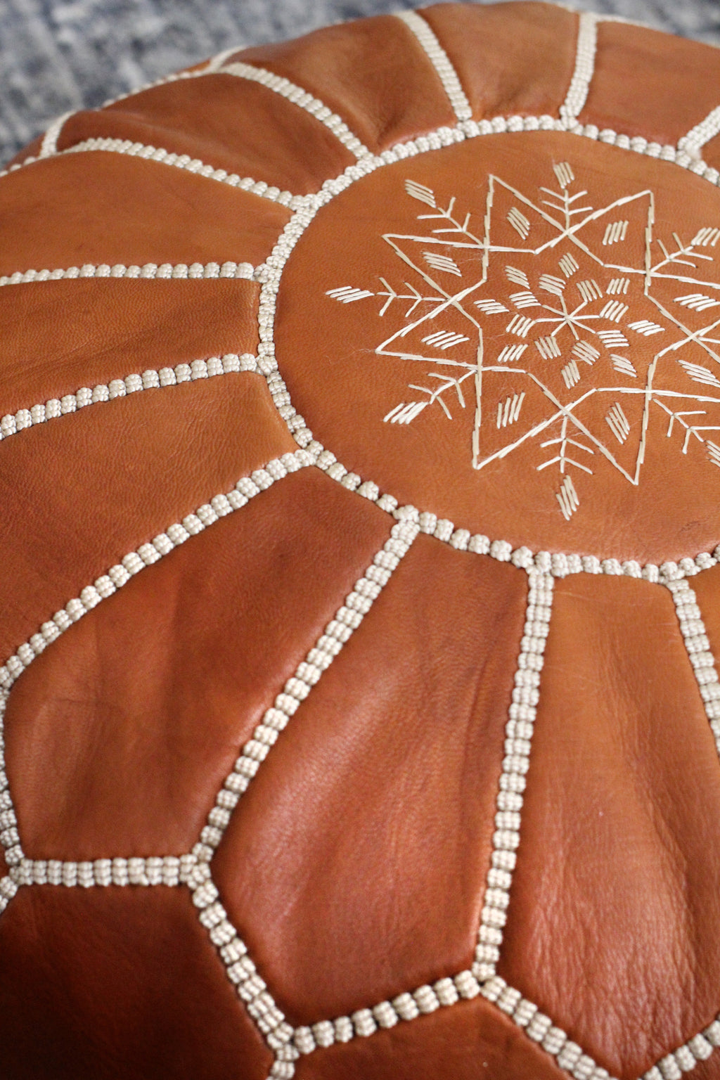 Brown leather ottoman with white embroidery on a textured surface