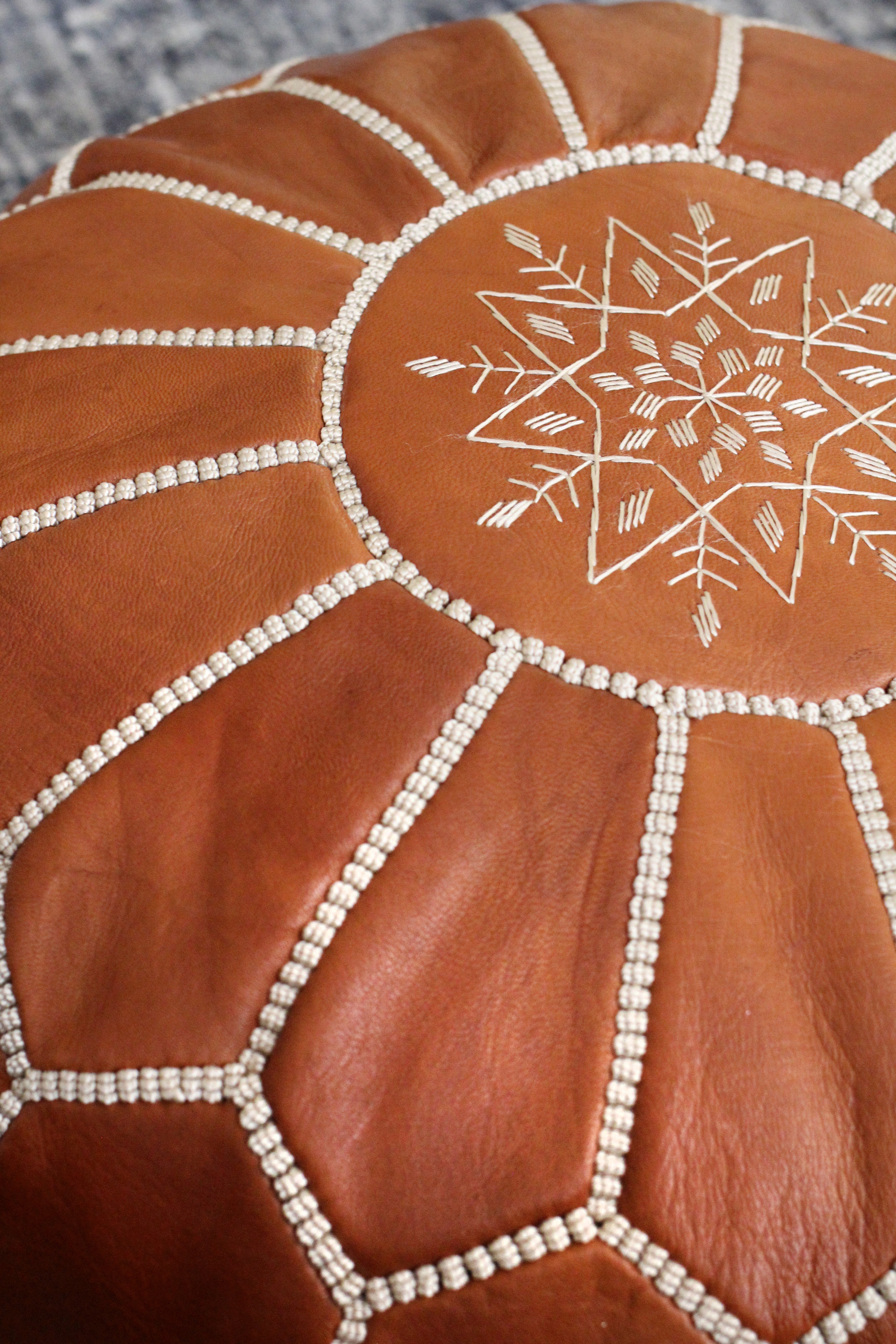 Brown leather ottoman with white embroidery on a textured surface