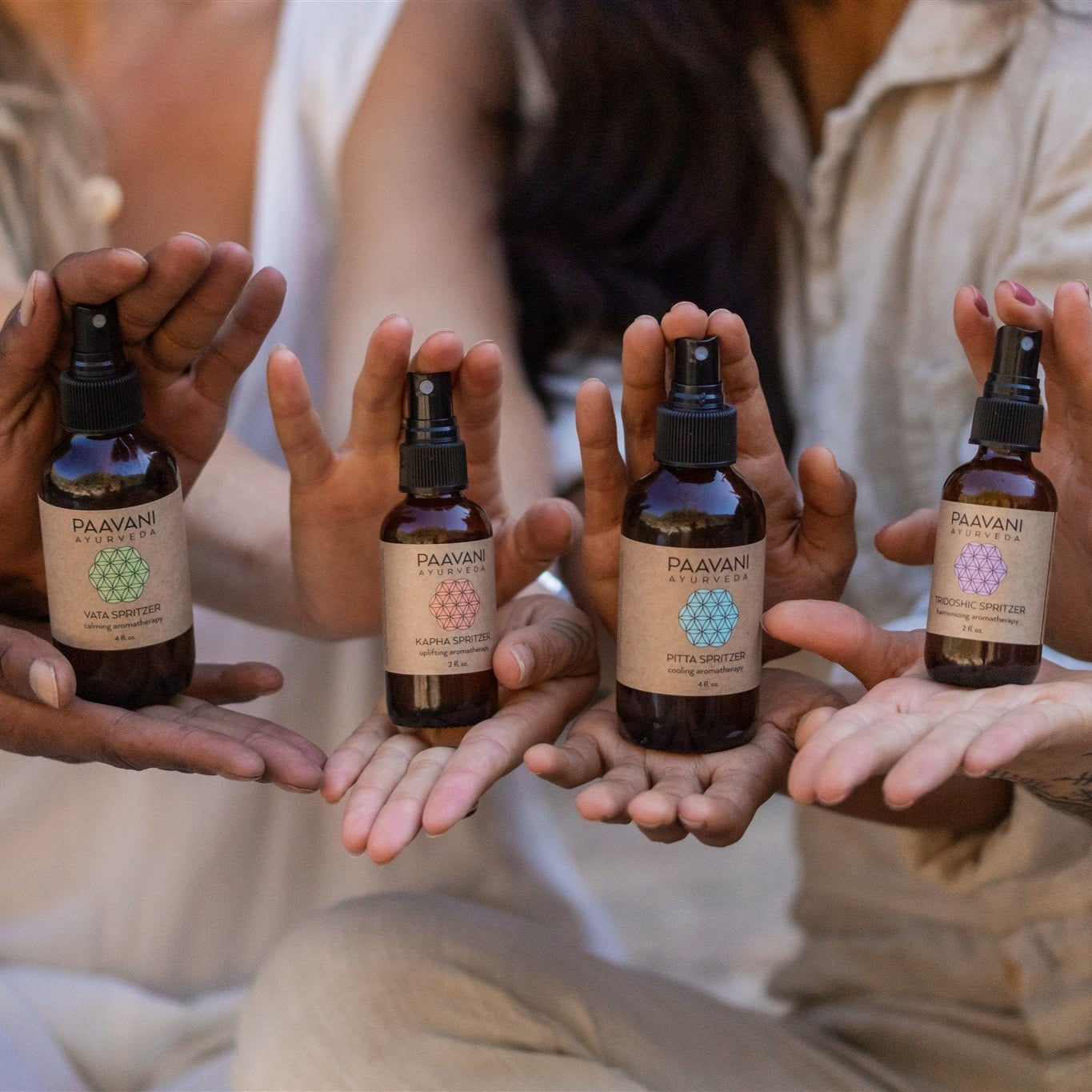 Four hands holding bottles of Paavani Ayurvedic products against a blurred background