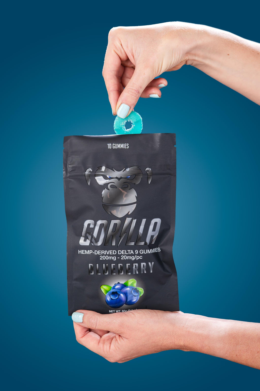 Hand holding a black Gorilla Gummies package with blueberry flavor against a blue background