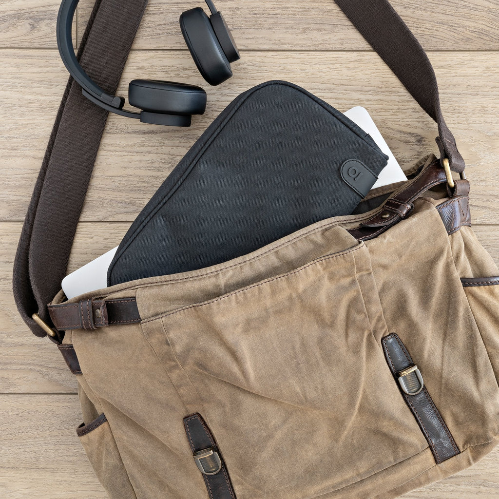 Brown leather bag with black laptop case and headphones on a wooden surface