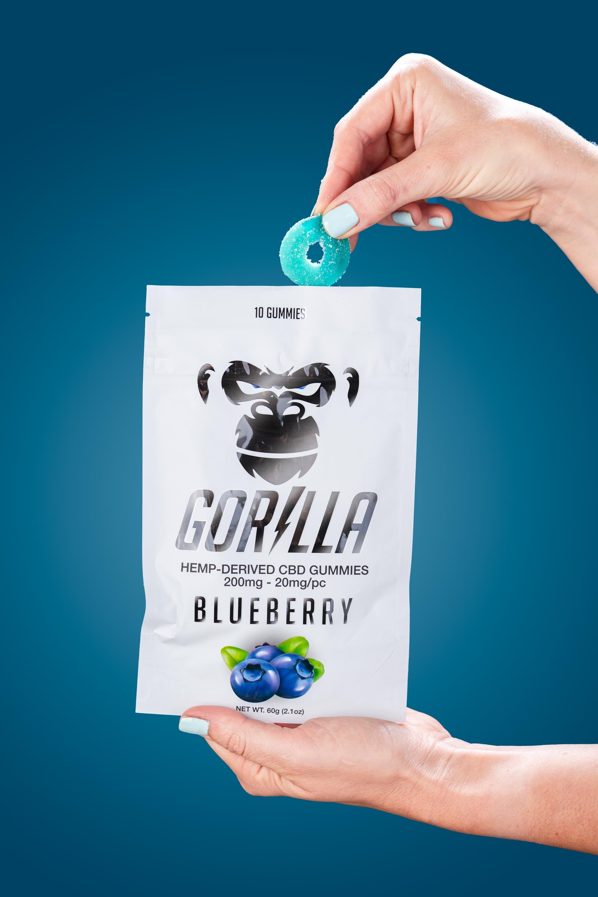 Hand holding a bag of Gorilla CBD gummies with a blueberry flavor against a blue background