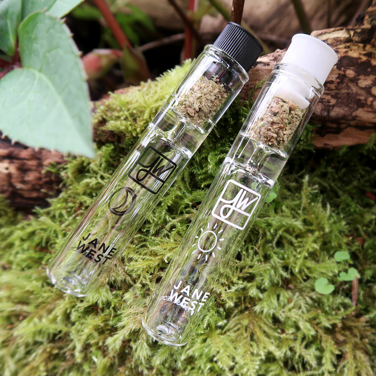 Two glass vials with black and white caps on a green moss background