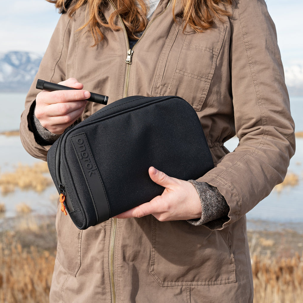 Person holding a black toiletry bag with a scenic background