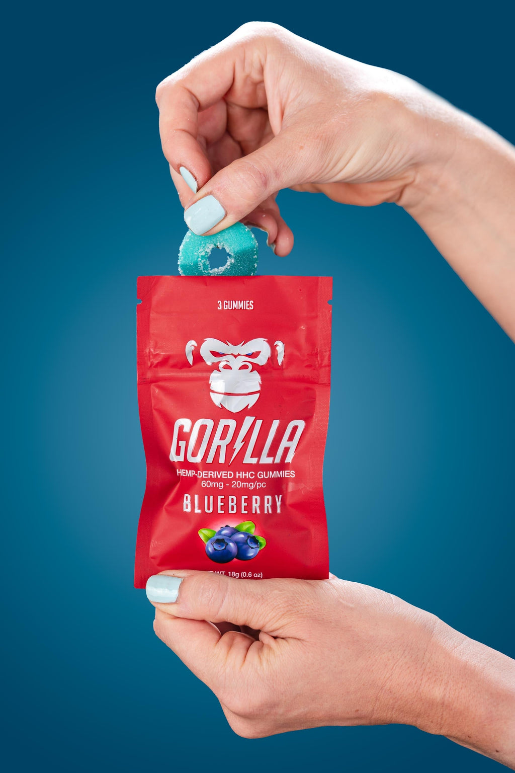 Hand holding a red Gorilla Gummies package with a blueberry flavor against a blue background