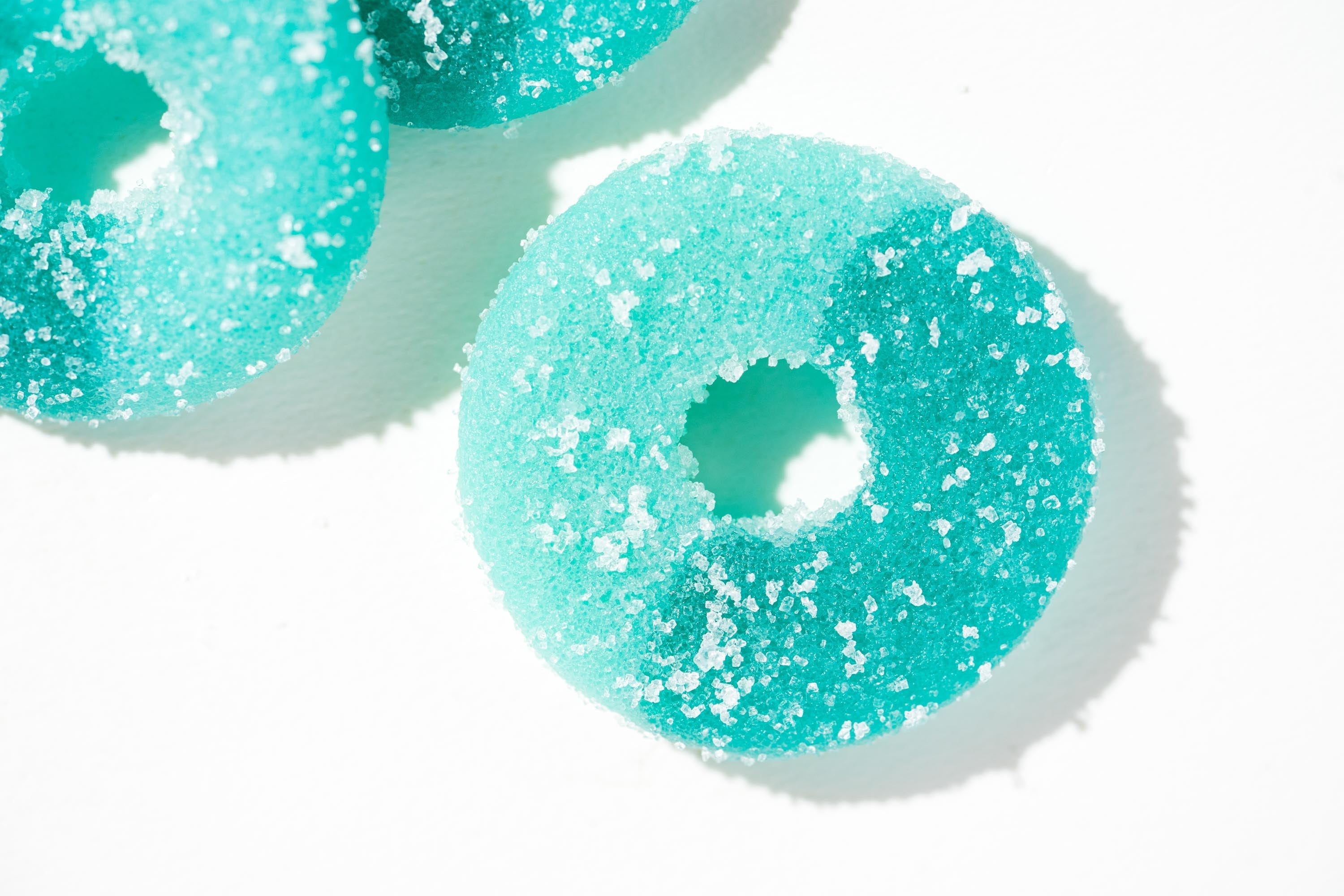 Turquoise gummy candy with white sprinkles on a white background