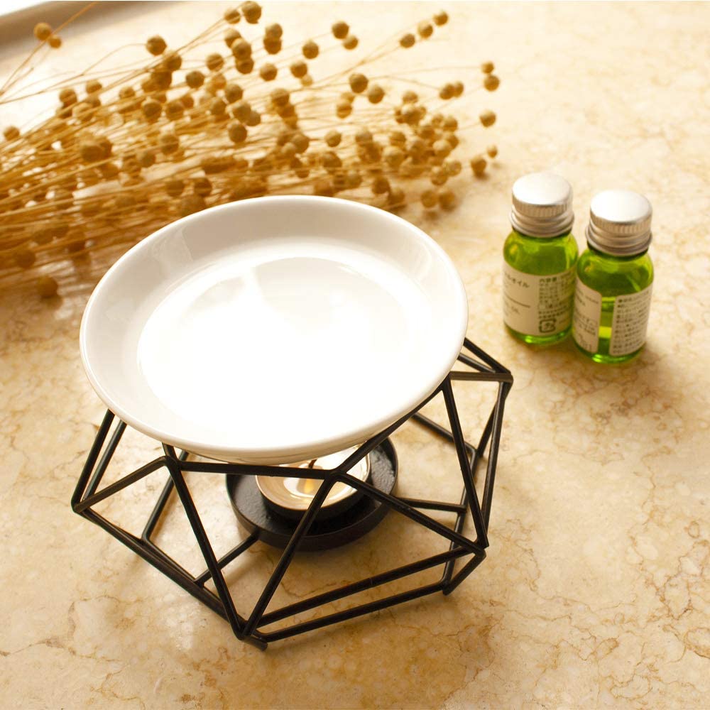 White dish on a black geometric stand with two green bottles in the background